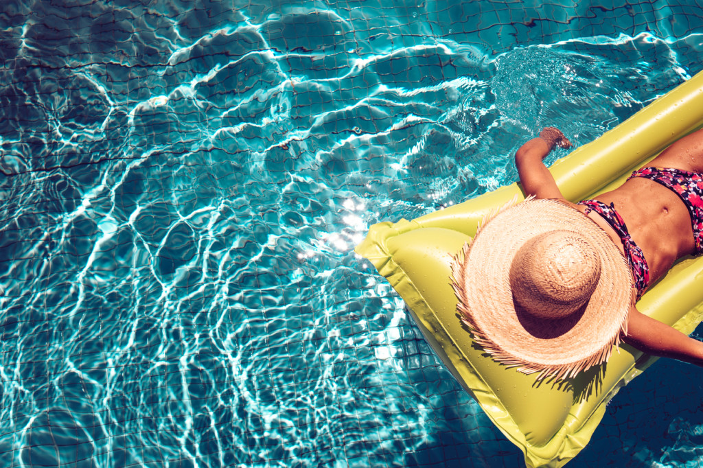 girl with straw hat on airbed swimming in blue pool